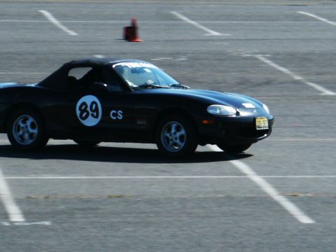 2001 Mercury Grand Marquis - A black convertible sports car with racing numbers is seen on a paved track with lane markings.