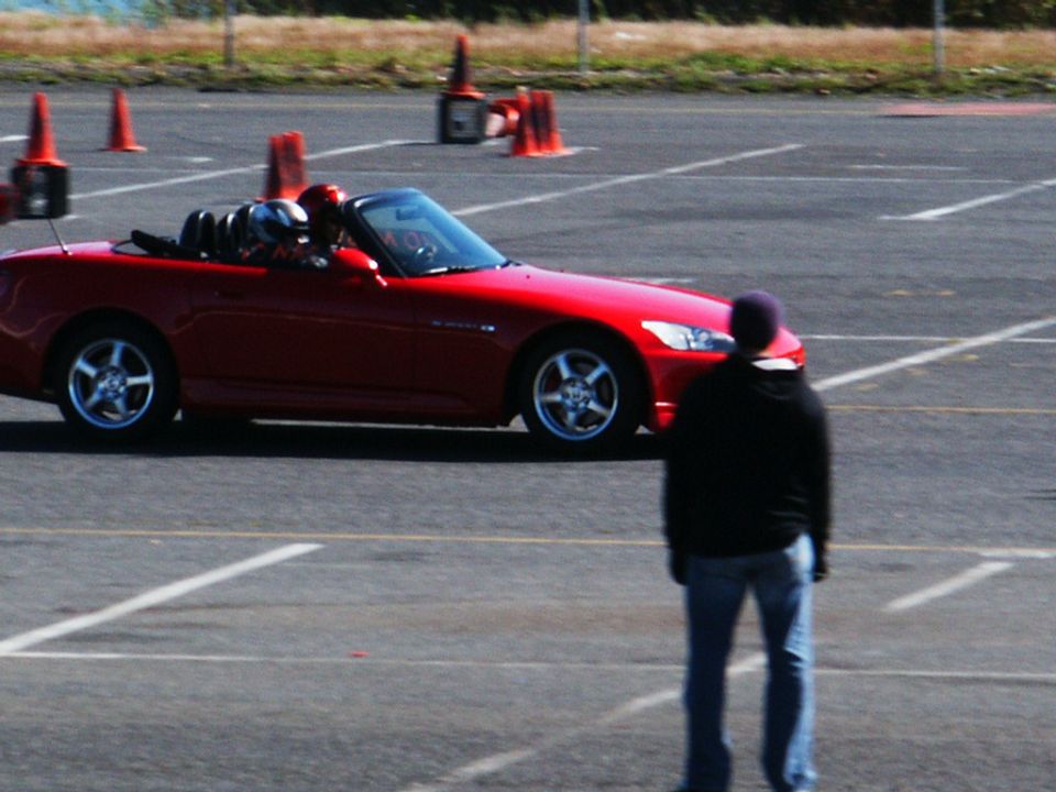 Red convertible sports car with two occupants, seen from the side at an autocross event