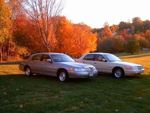 1996 Mercury Grand Marquis - Two full-size silver sedans parked side by side on a grassy lawn, with a Lincoln Town Car in the foreground and a Mercury Grand Marquis beh…