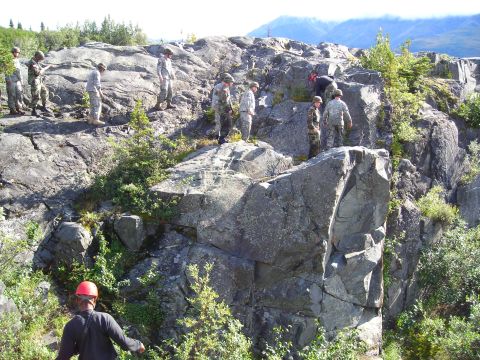 2003 Jeep TJ - A group of soldiers navigate a , rocky terrain under a clear sky, with mountains visible in the distance.
