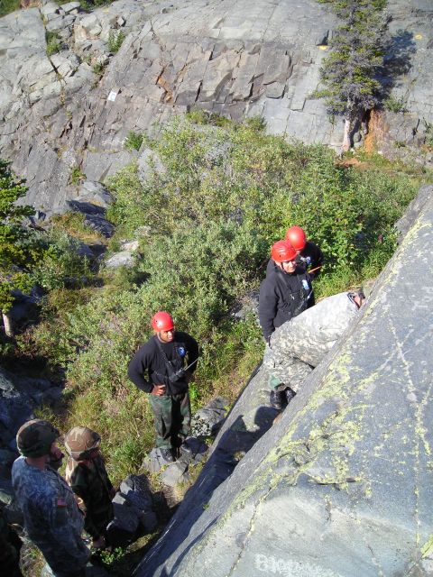 2003 Jeep TJ - People in military attire and helmets are gathered on a steep, rocky terrain with vegetation.