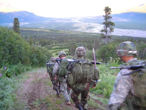 2003 Jeep TJ - A group of soldiers marches along a trail in a mountainous, forested landscape under a hazy sky.