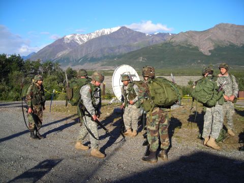 2003 Jeep TJ - A group of soldiers in camouflage uniforms and backpacks stand near a satellite dish, with a scenic mountain range visible in the distance…