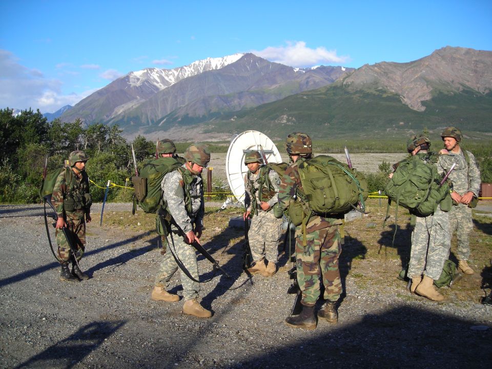 Soldiers gather near a satellite dish with mountains in the background