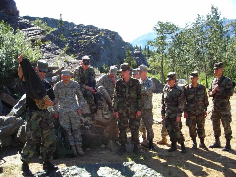 2003 Jeep TJ - A group of soldiers stand together in a mountainous, wooded area, some holding equipment.