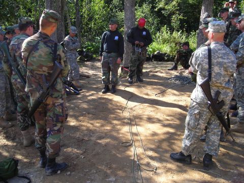 2003 Jeep TJ - A group of soldiers in camouflage uniforms gather outdoors in a wooded area, with ropes laid out on the ground.
