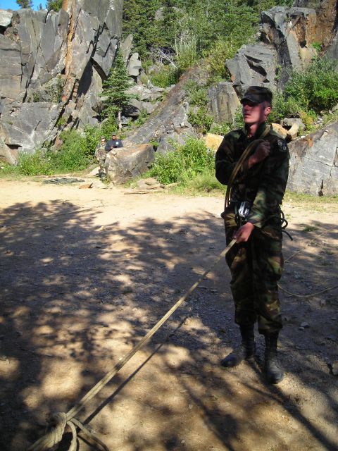 2003 Jeep TJ - A person in camouflage gear stands in a rocky outdoor area, holding a rope.
