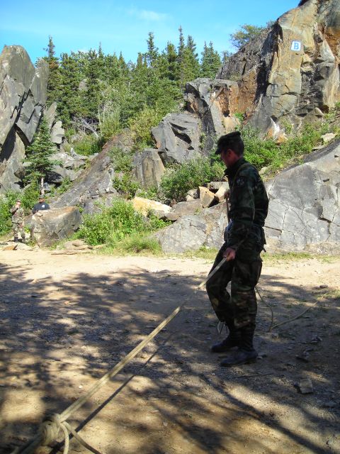 2003 Jeep TJ - A person stands in a rocky, wooded area, holding a rope near a cliff face with a marker 'B'.