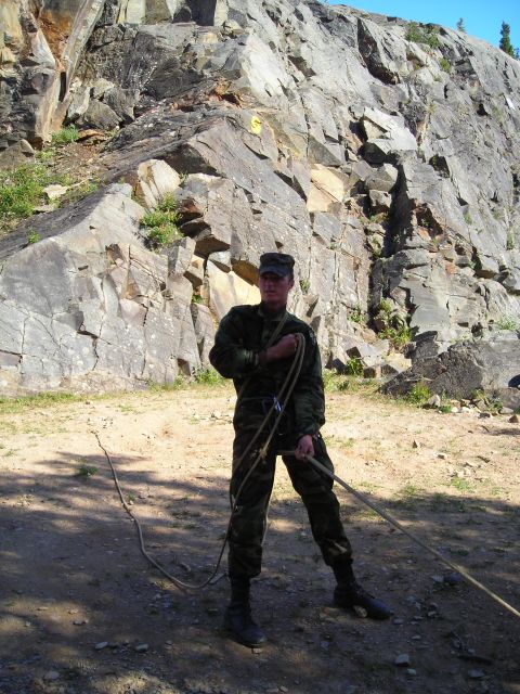 2003 Jeep TJ - A person in camouflage gear stands with a climbing rope in front of a large rock formation, likely preparing for an ascent.