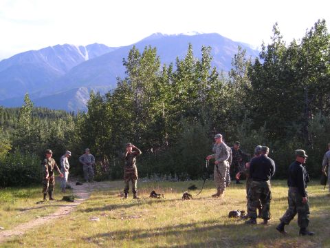 2003 Jeep TJ - A group of soldiers are gathered outdoors in a natural setting, with a mountain range visible in the distance.
