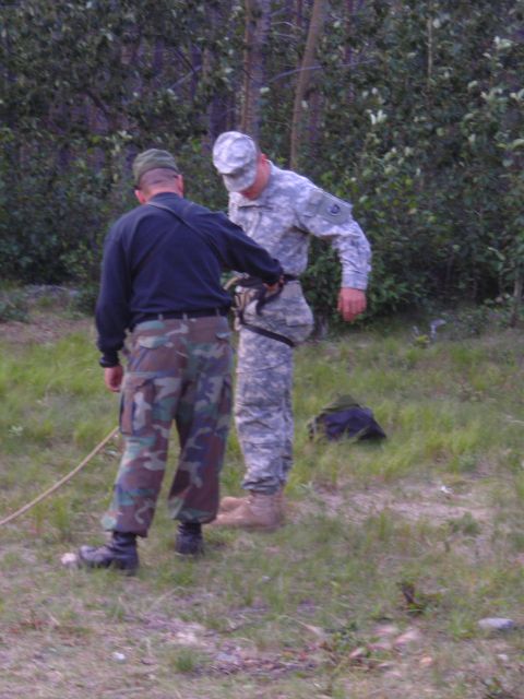 2003 Jeep TJ - Two men in military uniforms are outdoors, with one assisting the other with gear.