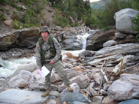 2003 Jeep TJ - A soldier stands in a rocky, natural environment next to a flowing stream and waterfall.