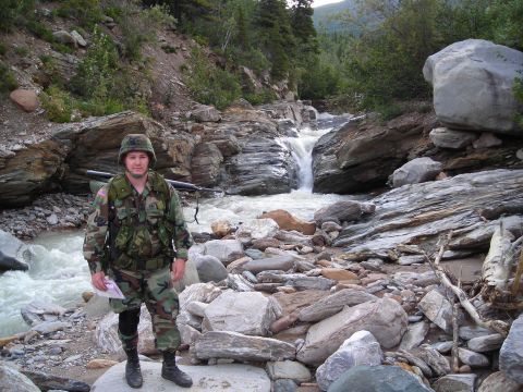 2003 Jeep TJ - A soldier stands in a , rocky landscape next to a flowing stream with a small waterfall.
