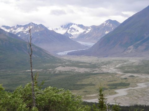 2003 Jeep TJ - A vast mountain valley landscape features a winding glacier and river, with snow-capped peaks in the distance under an overcast sky.