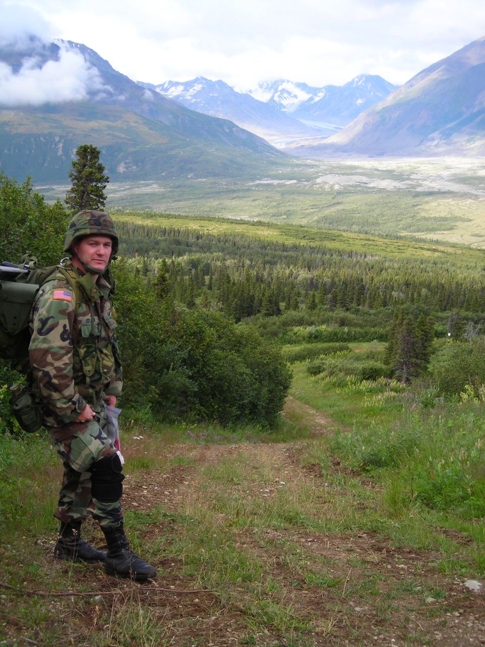 Soldier in camouflage uniform on a path with mountains and forest