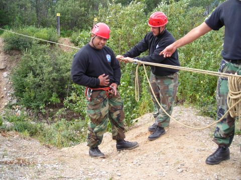 2003 Jeep TJ - Three individuals wearing safety helmets and camouflage attire are engaged with ropes in an outdoor setting.