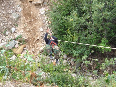 2003 Jeep TJ - A person uses a rope to descend a steep, rocky incline surrounded by vegetation.