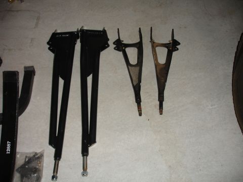1996 Ford Bronco - Four suspension control arms, two black and two rusty, are laid out on a concrete surface.