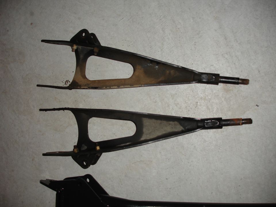 Two suspension control arms laid out on a concrete floor
