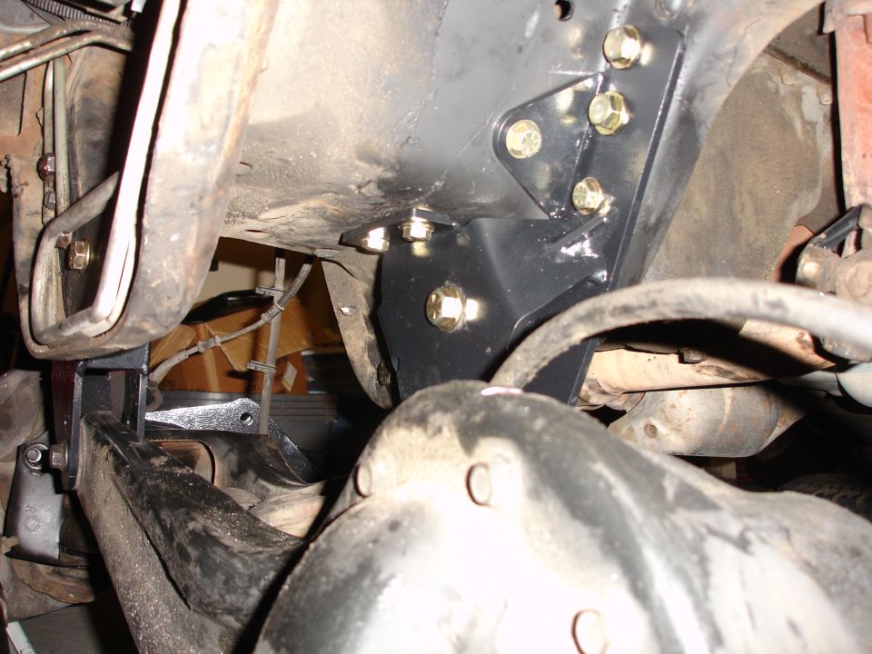 Black lift bracket bolted to vehicle frame with gold bolts. Suspension components visible