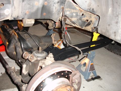 1996 Ford Bronco - Close-up view of the underbody suspension and brake components of a vehicle, supported by jack stands during maintenance.