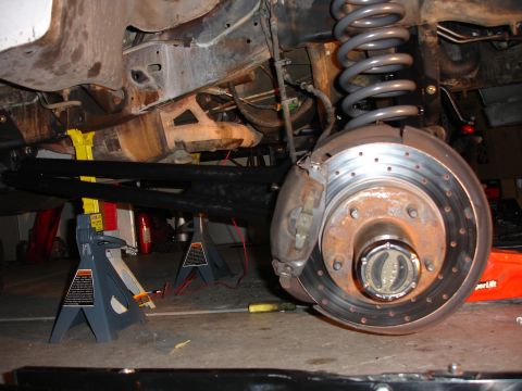 1996 Ford Bronco - Close-up view of a vehicle's suspension and brake system, with the vehicle elevated on jack stands.
