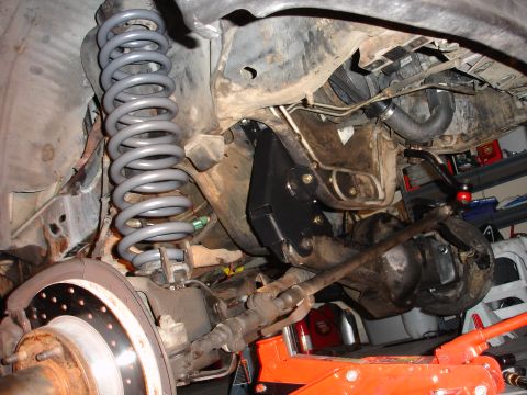 1996 Ford Bronco - Front suspension components of a 1996 Ford Bronco undergoing a lift installation, showing a new gray coil spring and black mounting bracket.