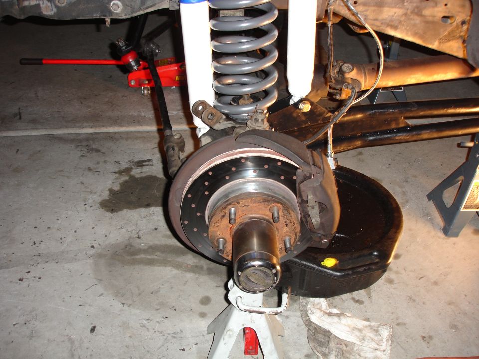 Vehicle front suspension with jack stands, coil spring, shock absorber, and brake rotor. Oil drain pan underneath
