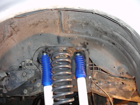 1996 Ford Bronco - Close-up view of the front suspension system, including coil springs and shock absorbers, within the wheel well.