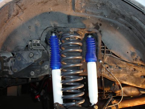 1996 Ford Bronco - Close-up view of suspension components, including shock absorbers and coil springs, within a vehicle's wheel well.