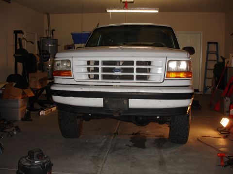 1996 Ford Bronco - Front view of a white Ford truck with a horizontal bar grille and blue emblem, parked in a garage.