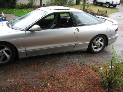 1994 Ford Probe - A silver coupe sits with its side window shattered, leaving glass scattered on the ground.