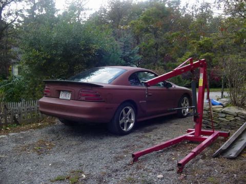 1995 Ford Mustang - A red 1995 Ford Mustang is parked next to a red cherry picker in a driveway.