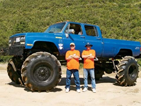 1990 Ford Bronco - This lifted pickup truck has massive tires and is shown with two people standing in front of it.