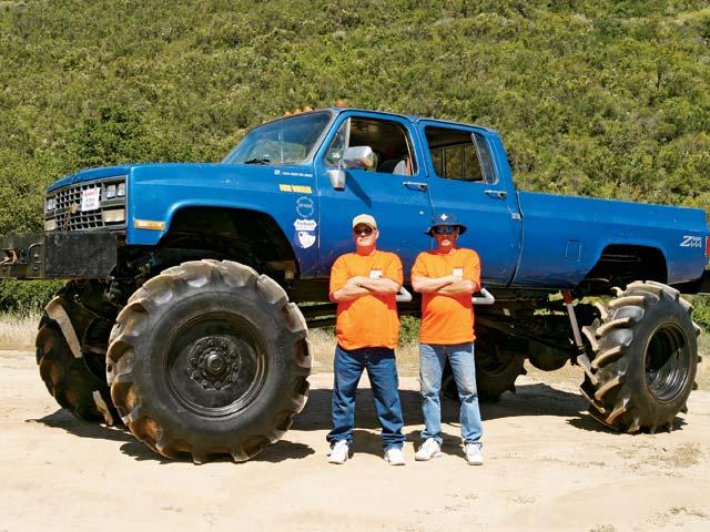 Blue lifted pickup truck with large tires, two men standing in front