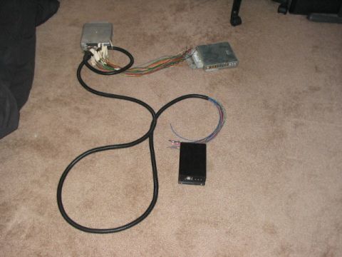 1991 Ford Bronco - Two engine control units and a wiring harness are laid out on a carpeted floor, along with a small black electronic box.