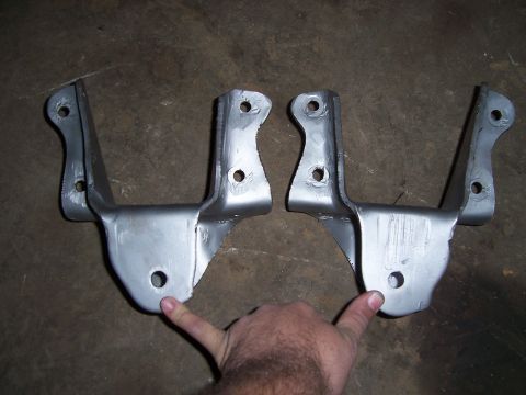 1983 Ford Bronco - Two metal brackets are shown on a concrete surface, likely automotive parts.