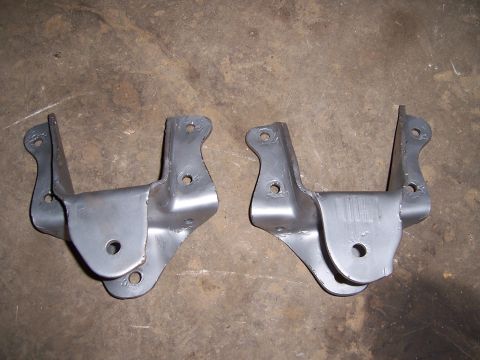 1983 Ford Bronco - Two metal brackets, likely for vehicle suspension, are shown on a concrete surface.
