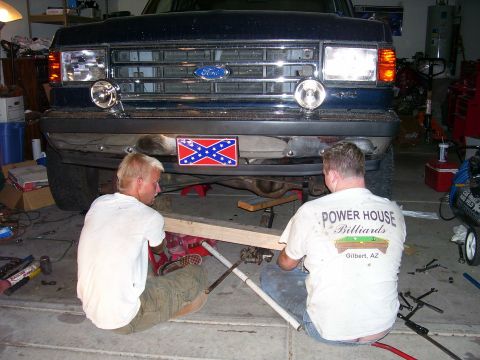 1991 Ford Bronco - Two men work on the underside of a 1991 Ford Bronco in a garage.