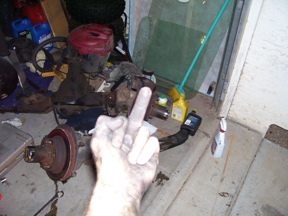 Greasy hand gesturing over garage floor strewn with axle, brake rotor and transfer case