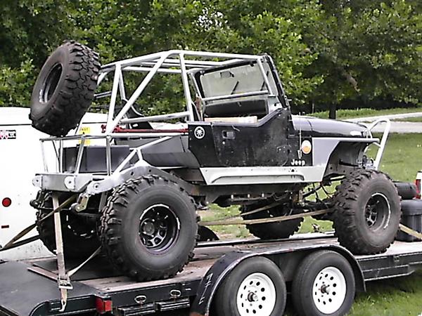 Modified Jeep with roll cage and large tires on a trailer. Text 'Jeep' visible on fender