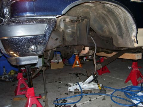 1991 Ford Bronco - Undercarriage of a blue vehicle being worked on, supported by jack stands with various tools scattered around.