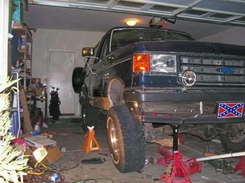 1991 Ford Bronco - A dark blue 1991 Ford Bronco is parked on jack stands inside a garage, undergoing maintenance.