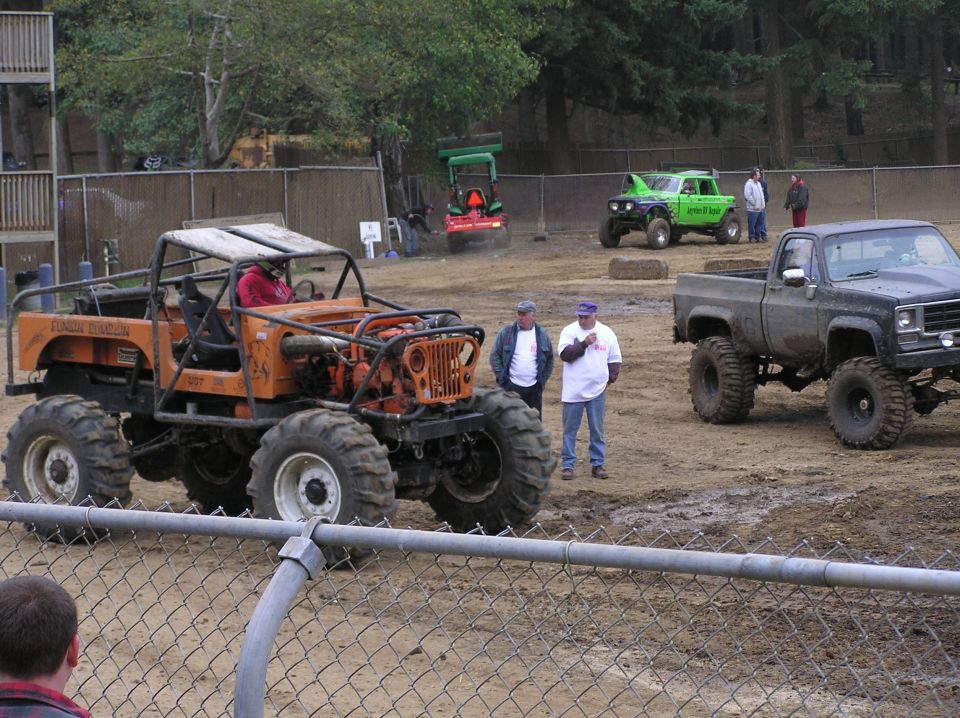 Modified orange jeep with large tires and roll cage, parked next to a lifted black pickup truck