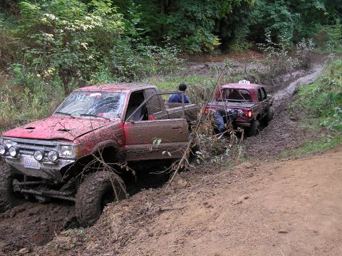 1995 Ford Bronco - Two off-road vehicles are stuck in deep mud on a trail surrounded by trees.