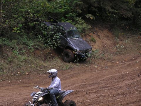 1995 Ford Bronco - An ATV rider passes a dark SUV that is stuck on a muddy hill in an off-road park.