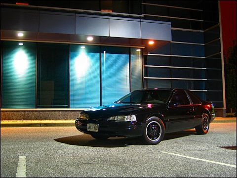 1997 Ford Thunderbird - A black coupe is parked in front of a building with blue-tinted windows at night.