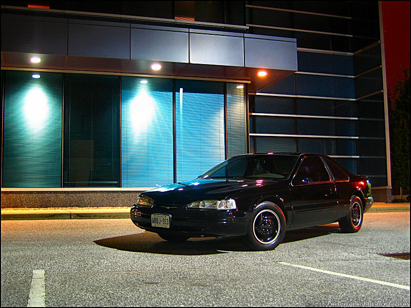 Black coupe parked in front of a modern building at night. License plate reads ARBJ-913