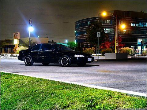 1997 Ford Thunderbird - A black coupe is parked on an asphalt lot at night, with a modern building in the background.