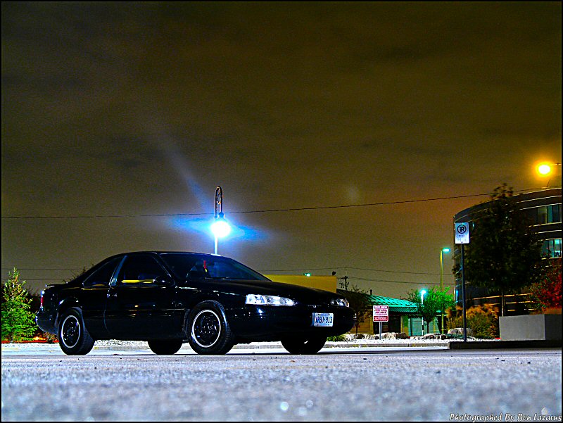 1997 Ford Thunderbird parked on asphalt at night, with a blue light illuminating the sky